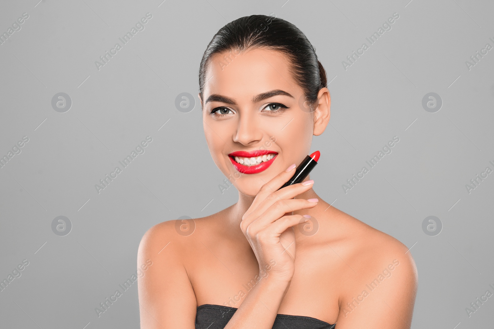 Photo of Young woman applying lipstick on color background