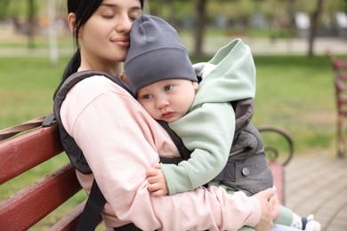 Photo of Mother holding her child in sling (baby carrier) on bench outdoors, closeup