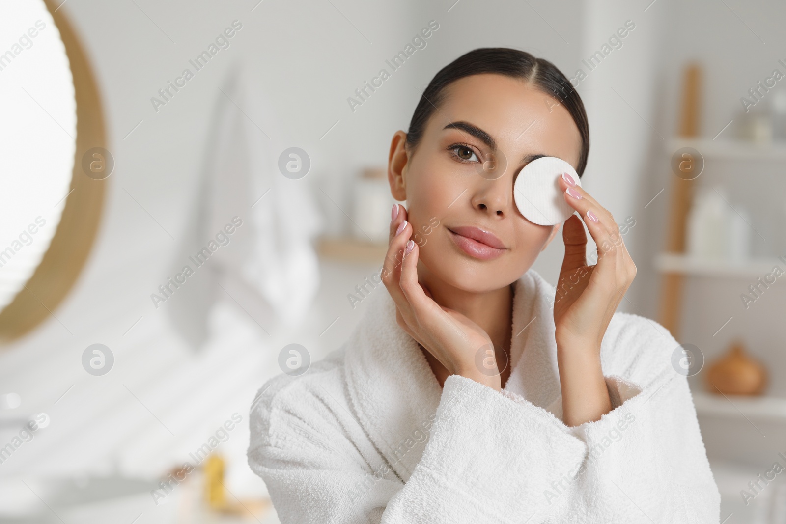 Photo of Beautiful woman removing makeup with cotton pad in bathroom, space for text