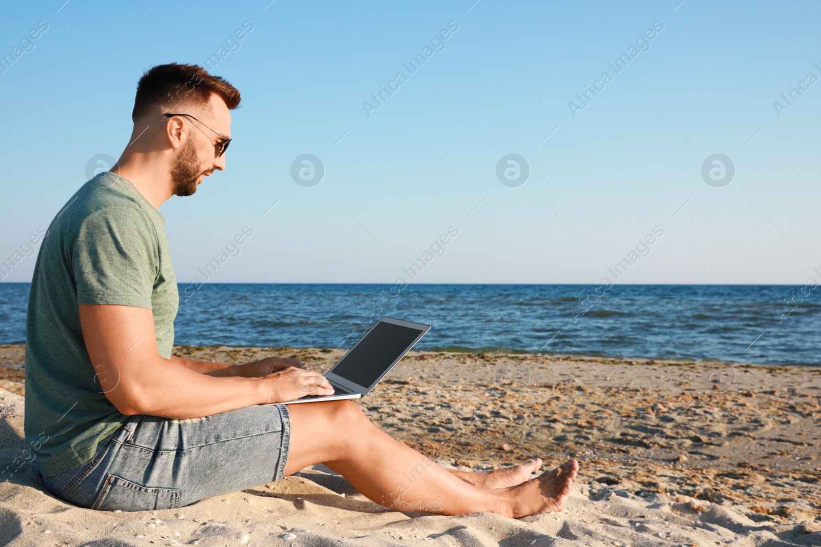 Photo of Man working with laptop on beach. Space for text