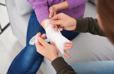 Photo of Young man applying bandage on woman's injured hand at home, closeup. First aid