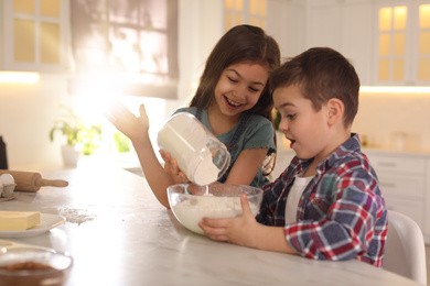 Cute little children cooking dough in kitchen at home