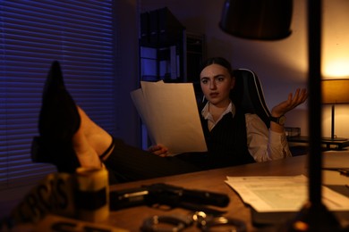 Photo of Professional detective working with documents at table in office at night