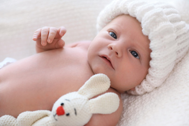 Photo of Cute newborn baby with toy in white knitted hat on plaid, closeup