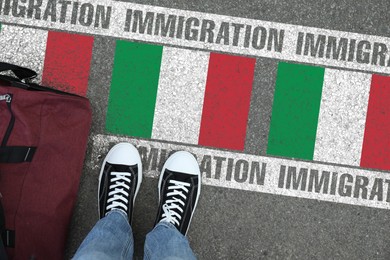 Image of Immigration. Man with bag standing on asphalt near flag of Italy, top view