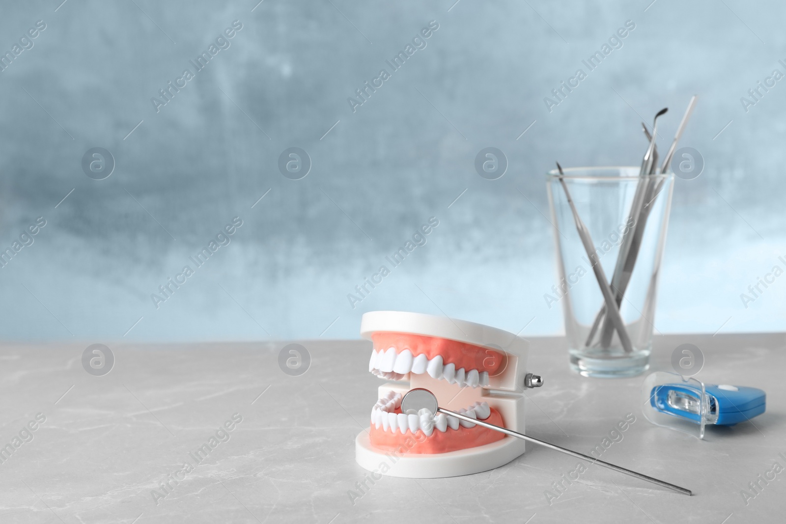 Photo of Typodont teeth, dentist mirror and whitening light lamp on table. Space for text