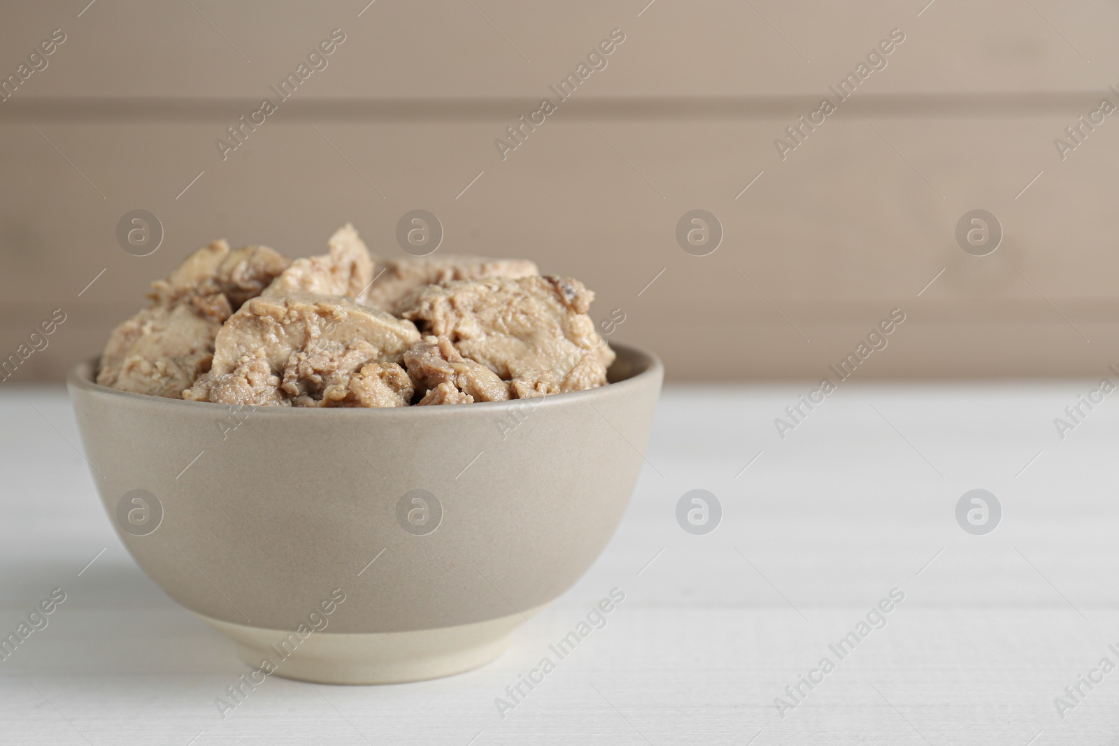 Photo of Bowl of tasty cod liver on white wooden table. Space for text
