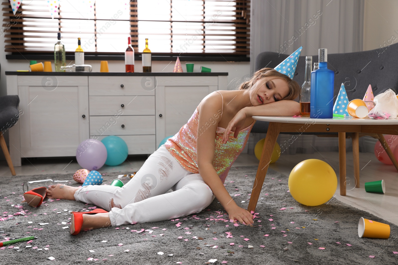 Photo of Young woman sleeping at table in messy room after party