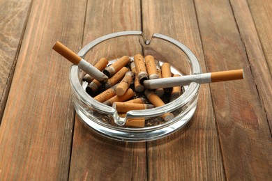 Photo of Glass ashtray with cigarette stubs on wooden table