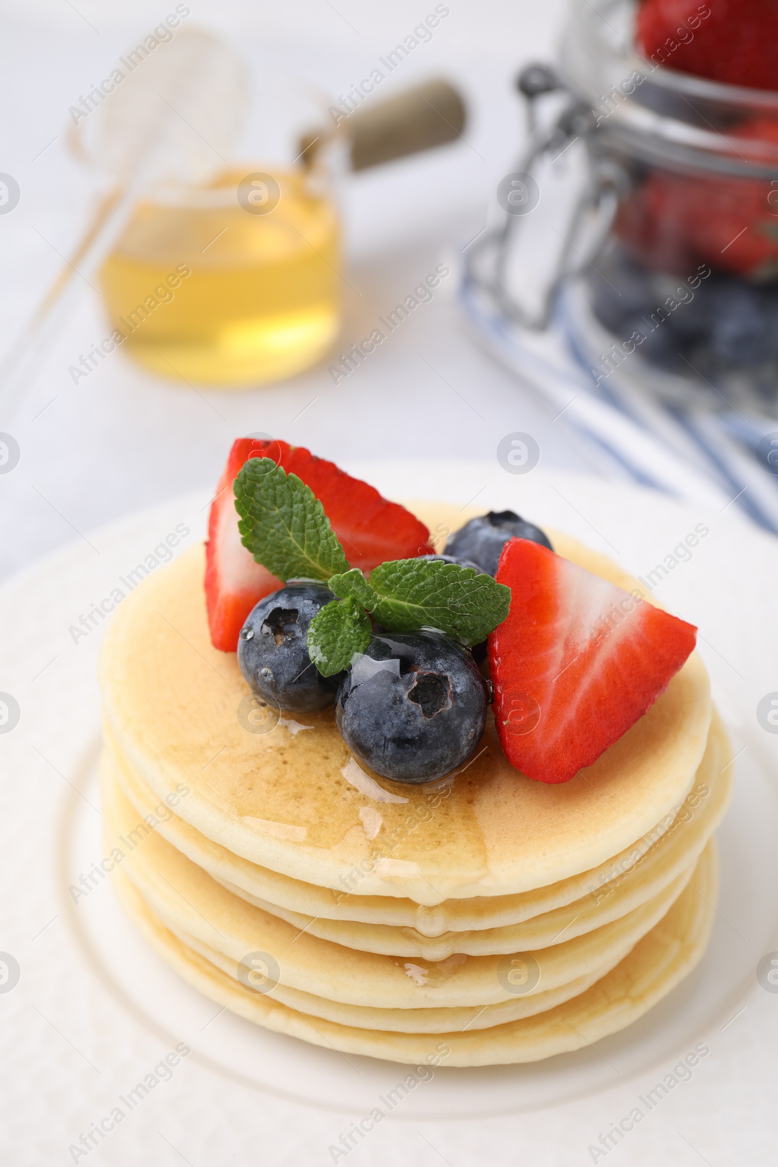 Photo of Delicious pancakes with strawberries, blueberries and honey on light table, closeup