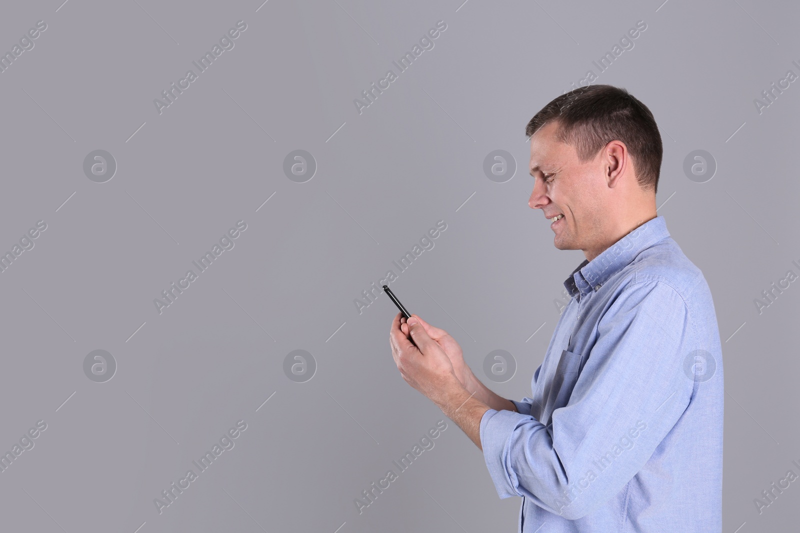 Photo of Man unlocking smartphone with facial scanner on grey background, space for text. Biometric verification