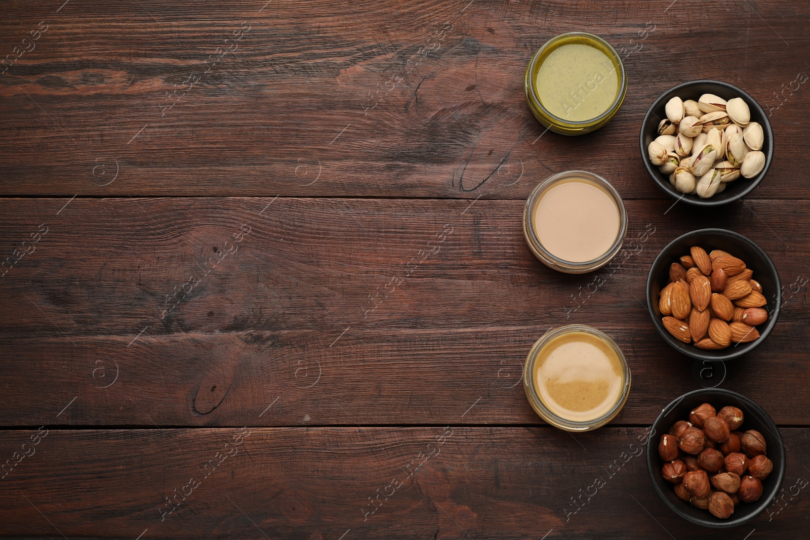 Photo of Different types of delicious nut butters and ingredients on wooden table, flat lay. Space for text