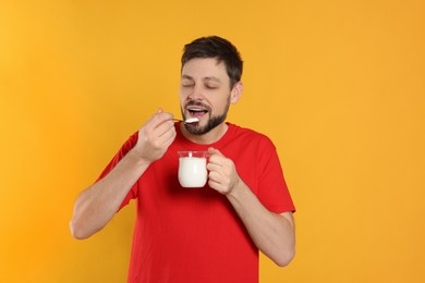 Photo of Handsome man eating tasty yogurt on orange background