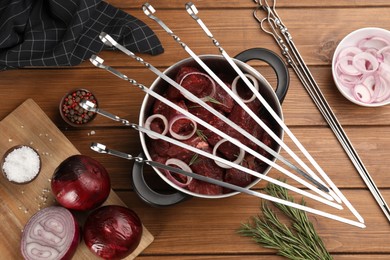 Flat lay composition with metal skewers and bowl of raw meat on wooden table