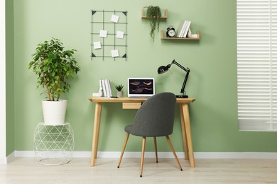 Photo of Workplace with modern laptop on wooden desk, potted plants and cosy chair at home