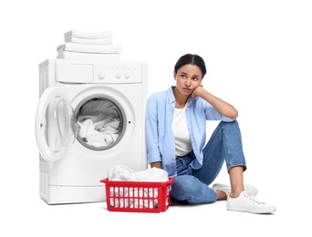 Beautiful woman sitting near washing machine with laundry on white background