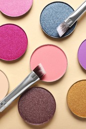 Different beautiful eye shadows and makeup brushes on beige background, flat lay