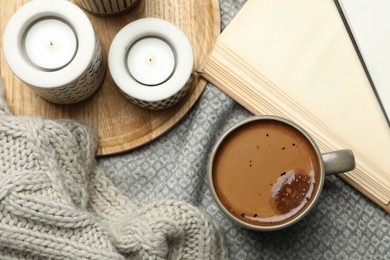 Photo of Cup of delicious hot winter drink and candles on grey fabric, flat lay. Winter drink