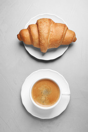 Tasty fresh croissant and coffee on light grey table, flat lay