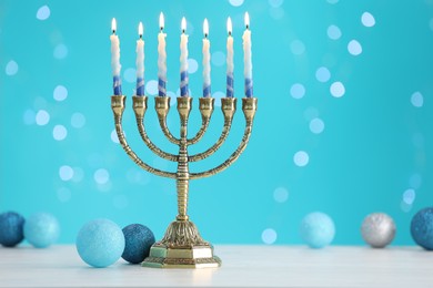 Photo of Hanukkah celebration. Menorah with burning candles and baubles on table against light blue background with blurred lights, space for text