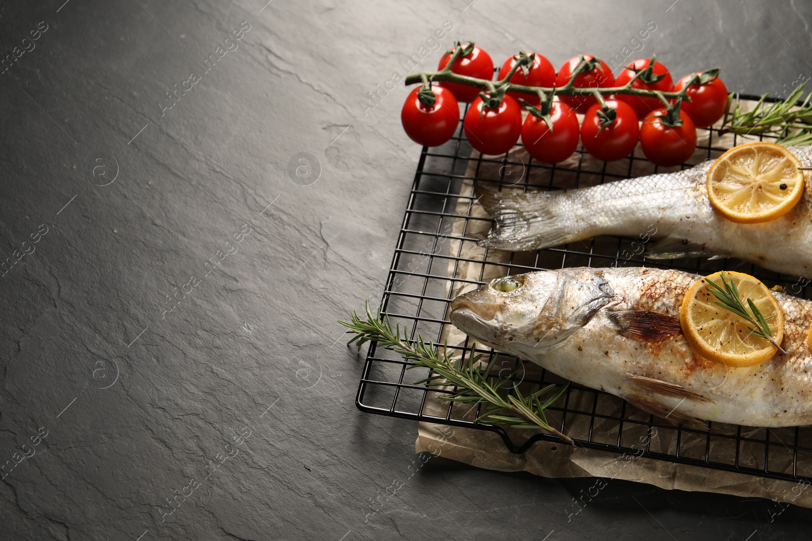 Photo of Baked fish with tomatoes, rosemary and lemon on black textured table, space for text