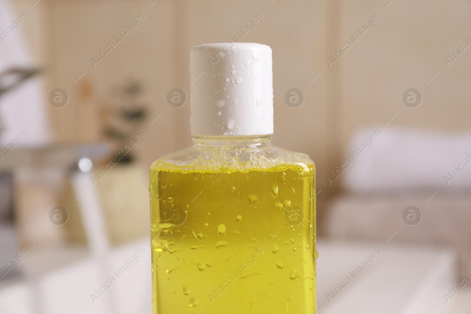 Photo of Fresh mouthwash in bottle with water drops indoors, closeup