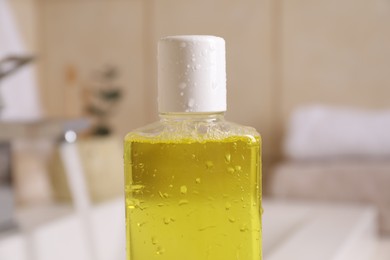 Fresh mouthwash in bottle with water drops indoors, closeup