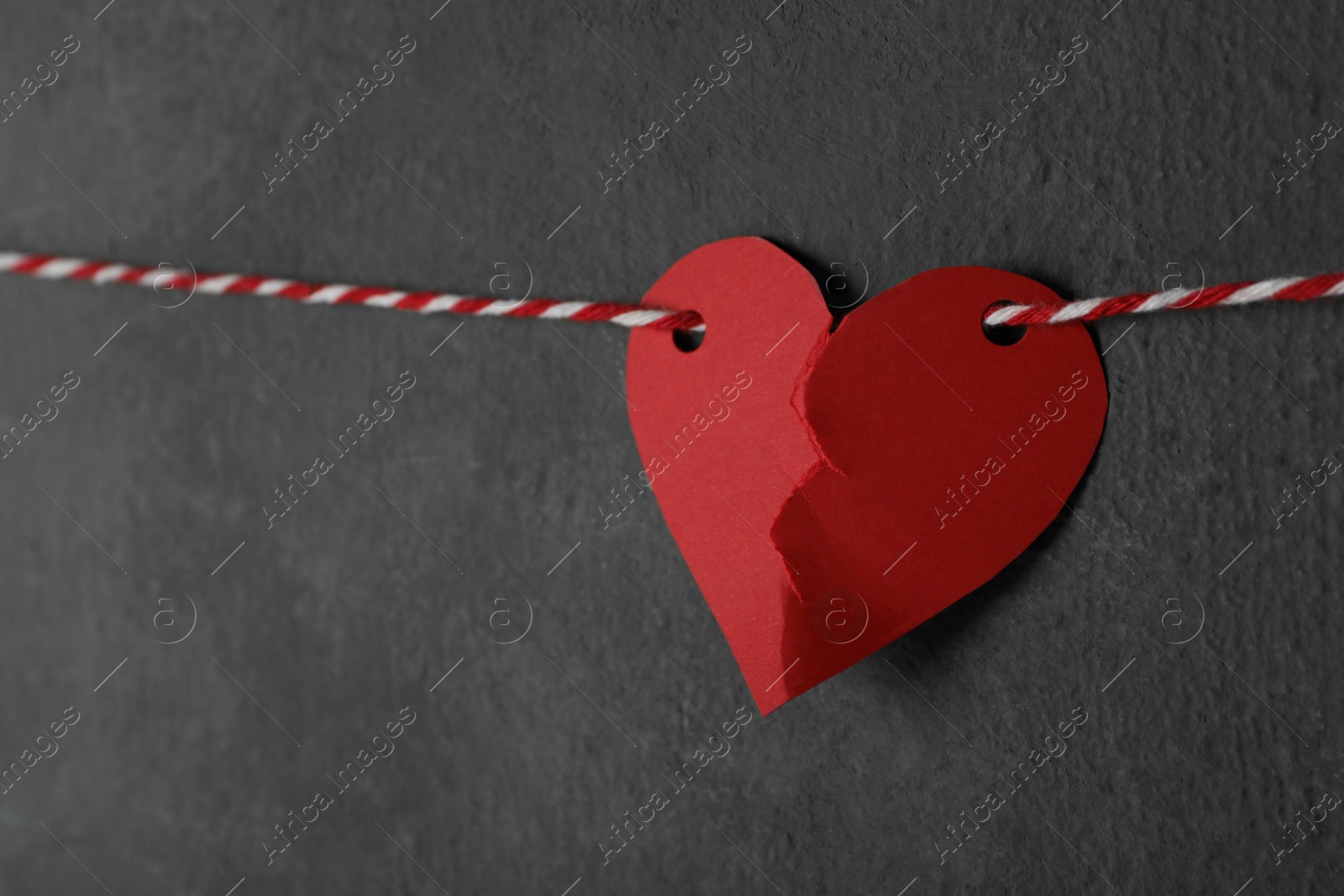 Photo of Broken red paper heart on rope near black wall, space for text. Relationship problems concept