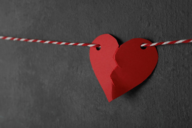 Broken red paper heart on rope near black wall, space for text. Relationship problems concept