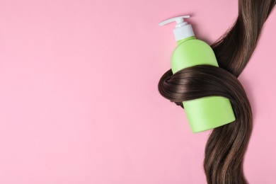 Shampoo bottle wrapped in lock of hair on pink background, flat lay with space for text. Natural cosmetic products