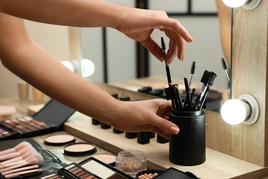 Photo of Professional makeup artist taking brush from holder at wooden table indoors, closeup
