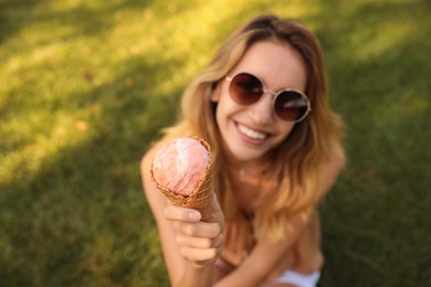 Photo of Happy young woman with delicious ice cream in waffle cone outdoors, focus on hand