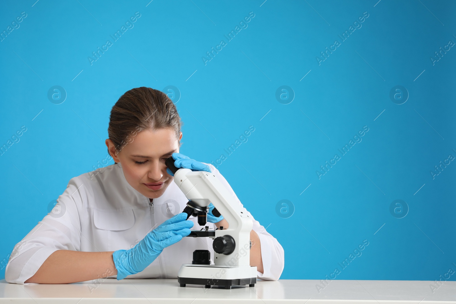 Photo of Scientist using modern microscope at table against blue background, space for text. Medical research