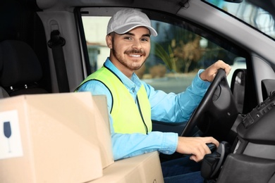 Photo of Young courier driving delivery van with parcels