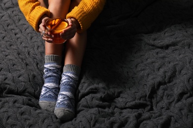 Photo of Woman in warm socks with cup of tea resting on knitted blanket, closeup. Space for text