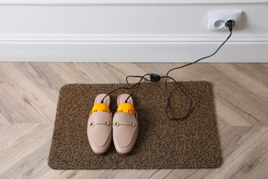 Photo of Pair of stylish shoes with modern electric footwear dryer on door mat indoors