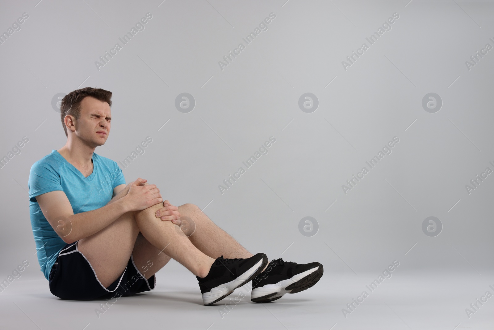 Photo of Man suffering from leg pain on grey background. Space for text