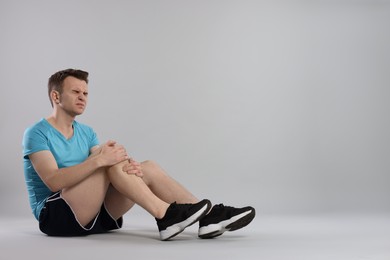 Photo of Man suffering from leg pain on grey background. Space for text