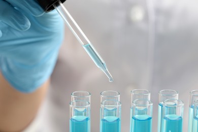 Scientist dripping liquid from pipette into test tube, closeup