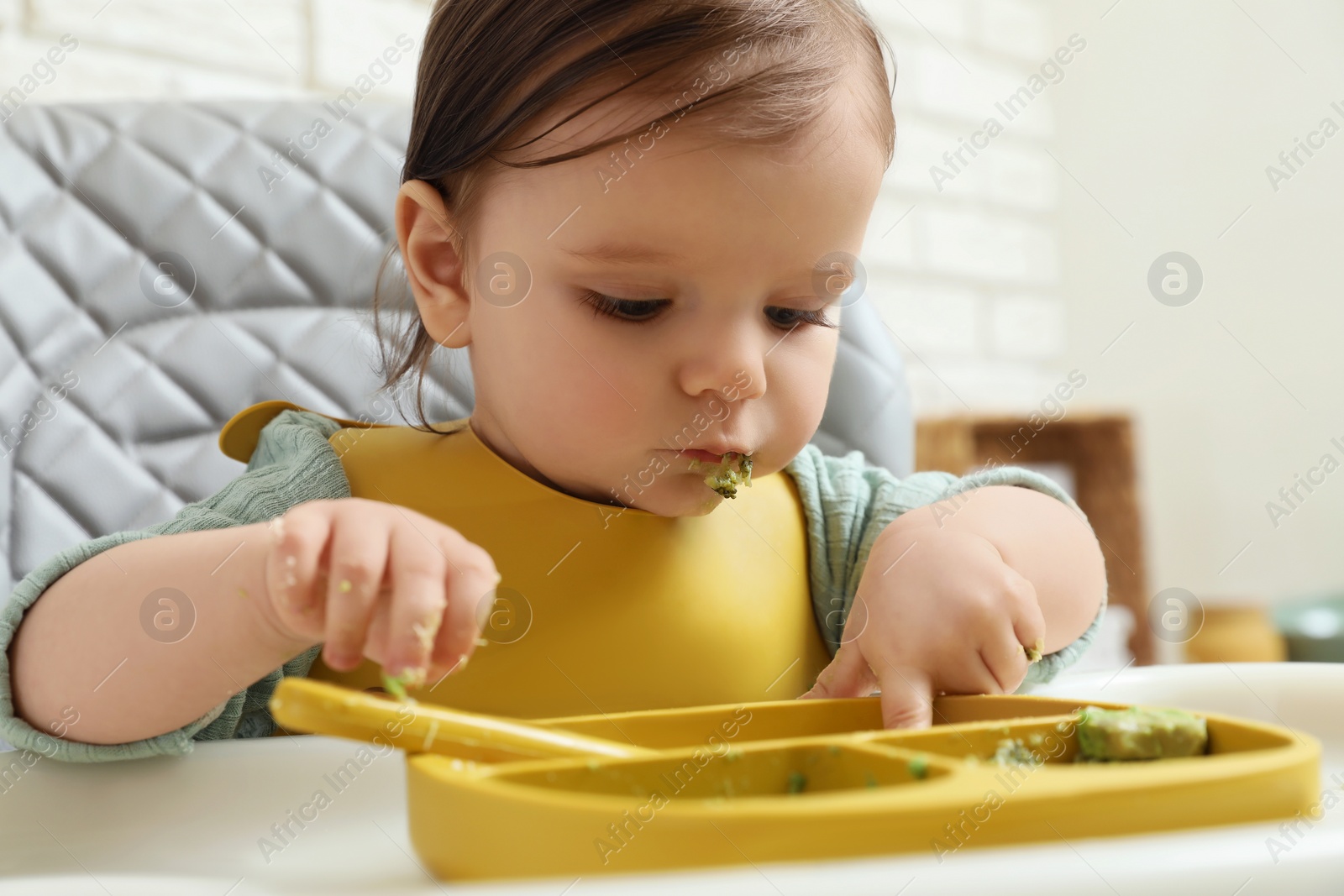 Photo of Cute little baby eating healthy food in high chair indoors