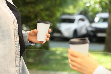 Photo of Women holding takeaway paper cups outdoors, closeup. Coffee to go