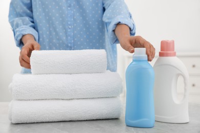 Woman with bottles of detergents and clean towels at light grey marble table, closeup