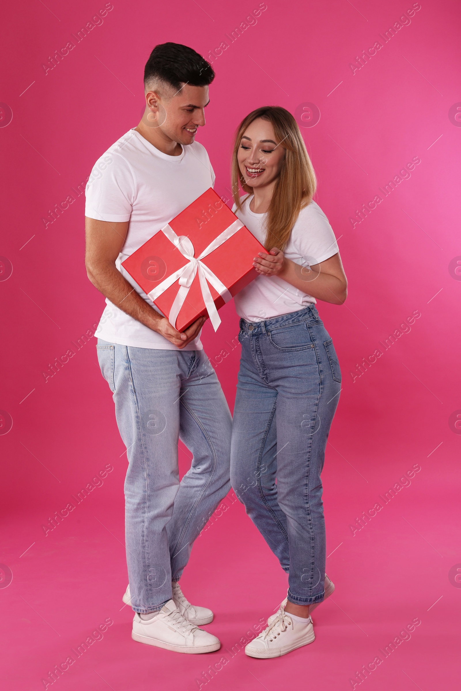 Photo of Man surprising his girlfriend with gift on pink background. Valentine's day celebration