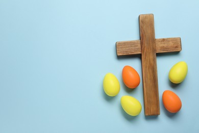 Wooden cross and painted Easter eggs on light blue background, flat lay. Space for text