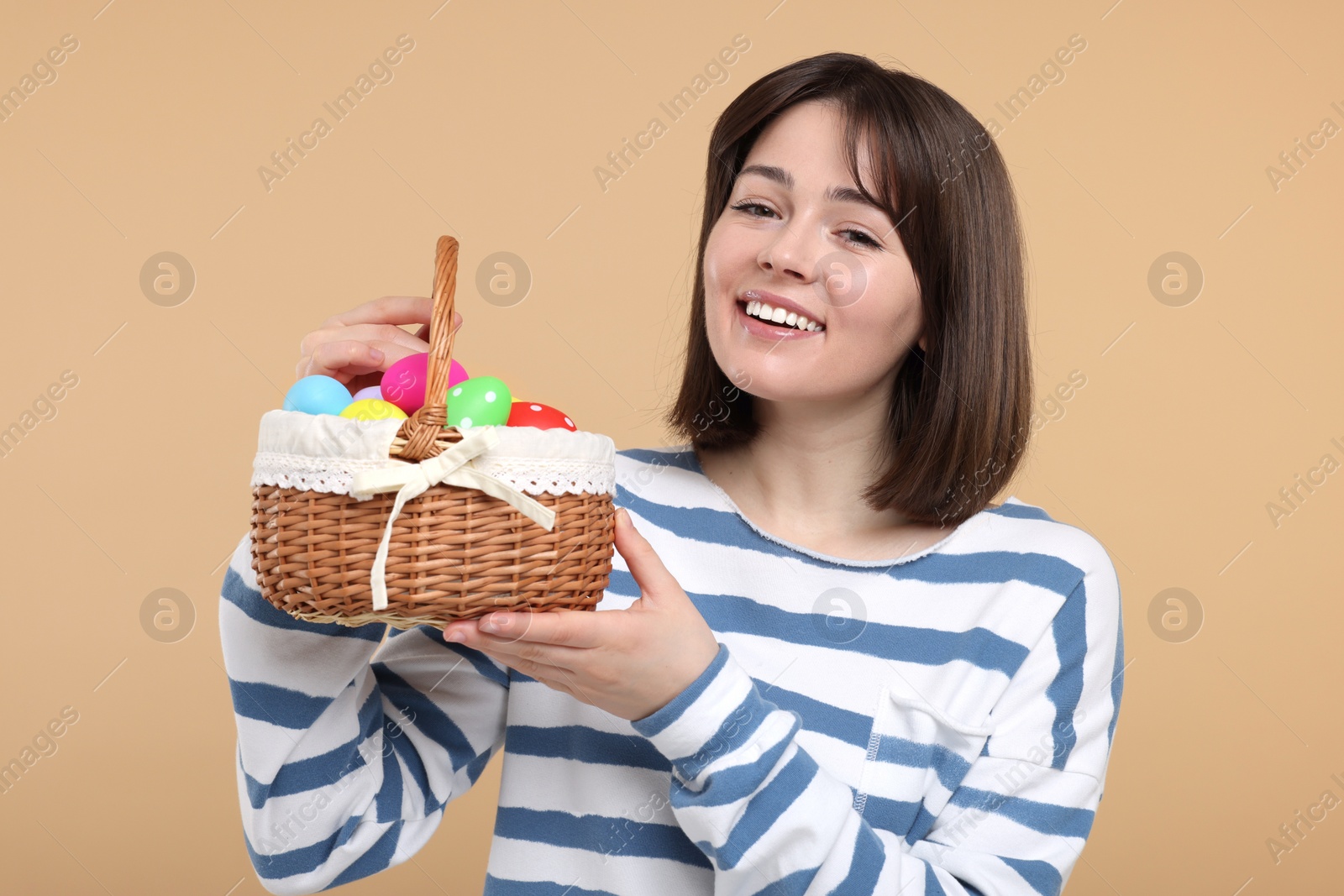 Photo of Easter celebration. Happy woman with wicker basket full of painted eggs on beige background