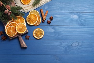 Photo of Dry orange slices, anise stars and fir tree branches on blue wooden table, flat lay. Space for text