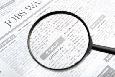 Photo of Looking through magnifying glass at newspaper, closeup. Job search concept