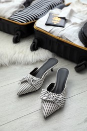 Stylish shoes near open suitcase packed for trip on floor