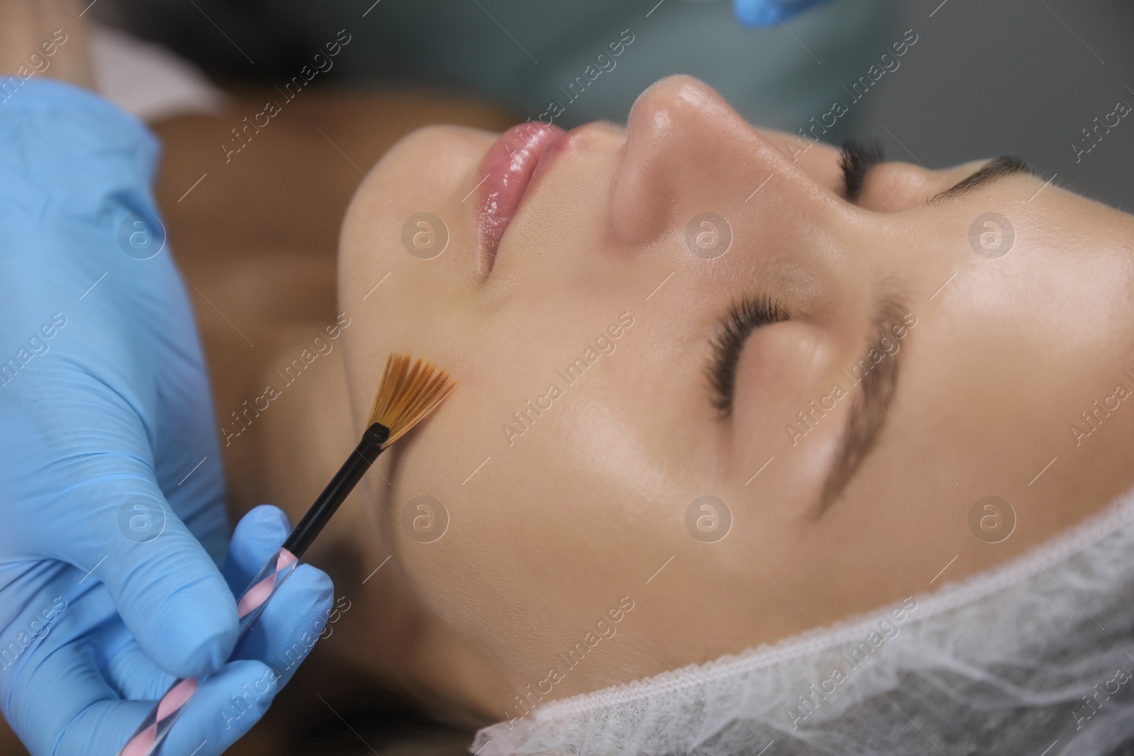 Photo of Cosmetologist applying chemical peel product on client's face in salon, closeup