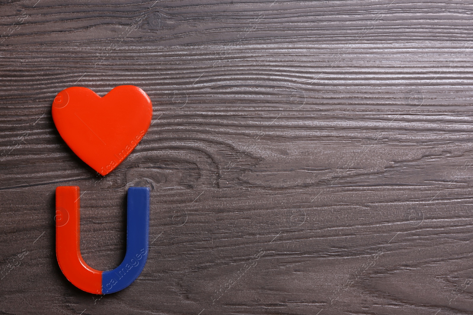 Photo of Red and blue horseshoe magnet with decorative heart on dark grey wooden background, flat lay. Space for text